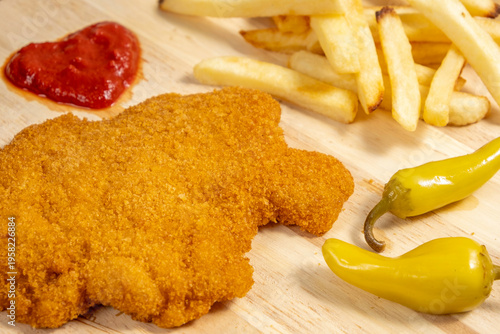 Tasty snack background. Chicken schnitzel, pickled peppers, potato chips, ketchup on wooden platter.