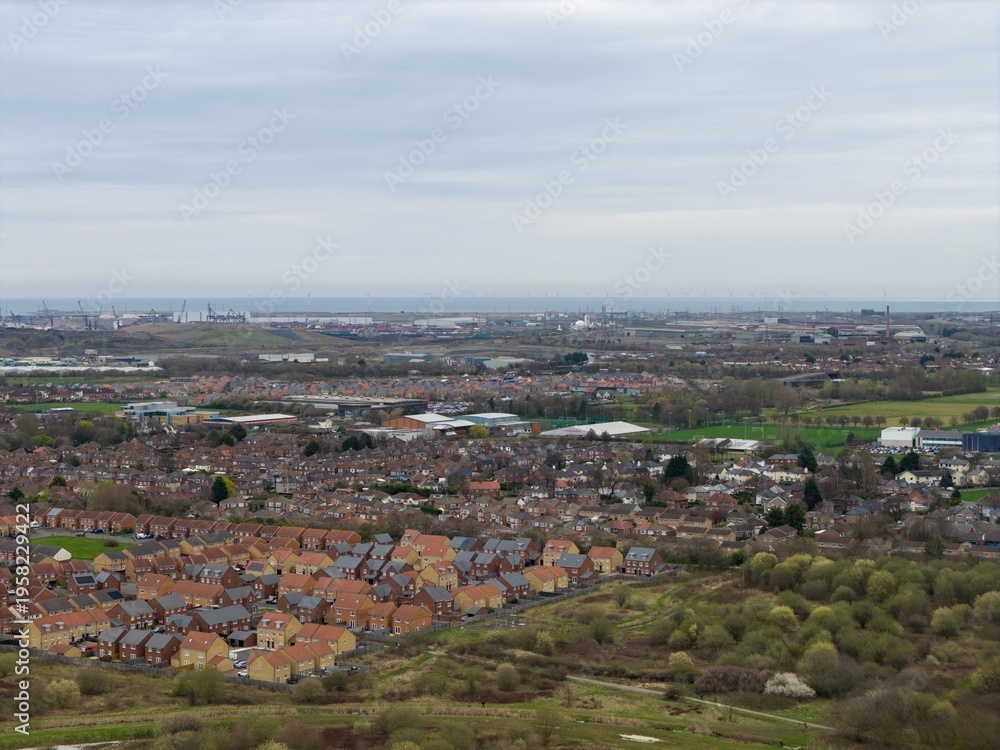 Fototapeta premium Aerial view of the Middlesbrough housing and industrial port area with wind turbines and coastline showing contrast between residential streets and heavy industry in the daytime in early spring