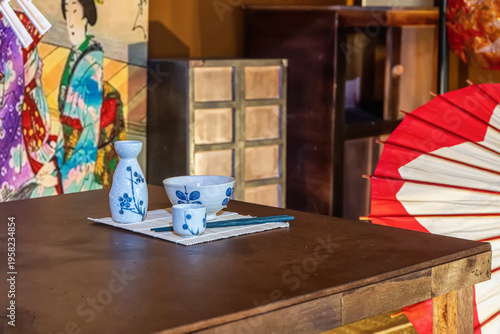 A traditional Japanese sake set on a table with a colorful Japanese umbrella and screen in background.