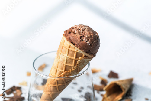 Closeup of waffle cone with chocolate ice cream in glass with chocolate pieces on light background