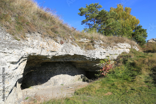 Photos Natural cave entrance carved into a rocky hillside with dry grass and trees