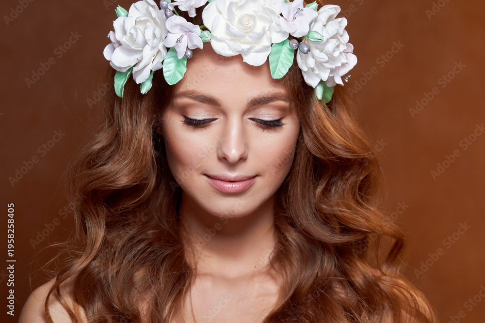 Naklejka premium Close-up of a beautiful portrait of a young girl with a flower wreath in her hair. She is wearing a delicate flower crown with green leaves. The concept of beauty, spa, manicure, and skin care