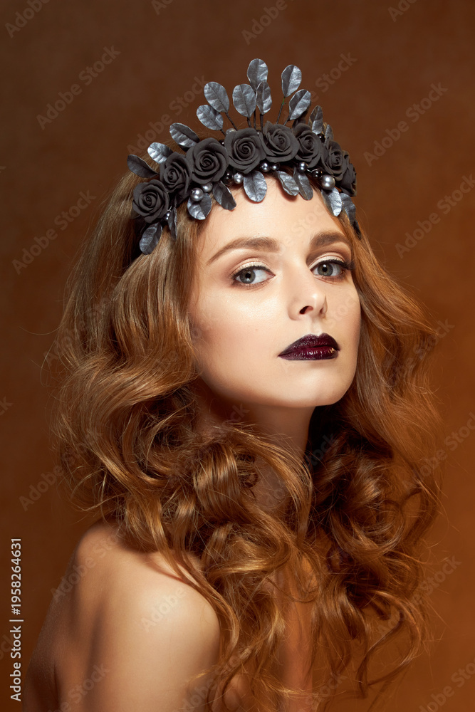 Fototapeta premium Close-up portrait of a beautiful young girl with a flower wreath in her hair. She wears a delicate flower crown with dark leaves. Beauty, spa, manicure and skin care concept