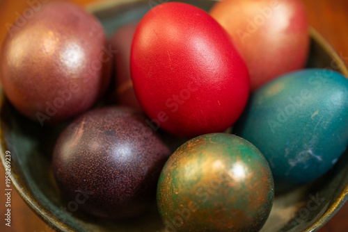 Foto a brown ceramic bowl filled with dyed easter eggs in shades of vibrant red, deep purple, and metallic green-bronze, resting on a dark wooden surface under warm natural light