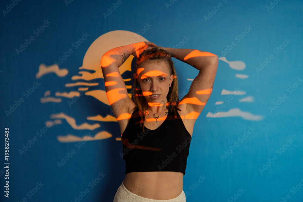 Obraz premium Woman posing with abstract sunset light projection on blue wall