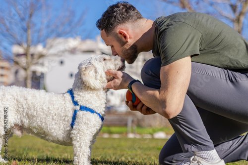 Man showing affection to white dog in park, sharing tender moment, pet care activity