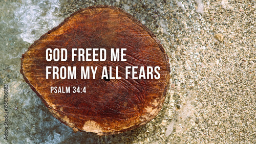 A close-up shot of a bible inspirational quote 'God Freed Me From My All Fears' from Psalm 34:4 on a wooden slice against a textured stone background