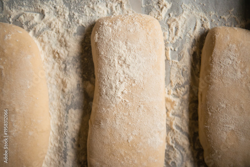 Close-up of raw ciabatta dough generously dusted with flour on a baking surface before going into the oven. Artisan bread preparation process, rustic style, soft natural lighting.