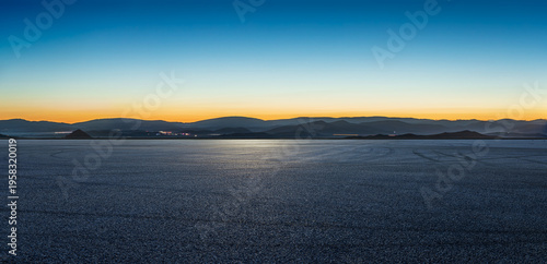 Vast empty asphalt pavement with mountain silhouettes under a clear blue hour sky