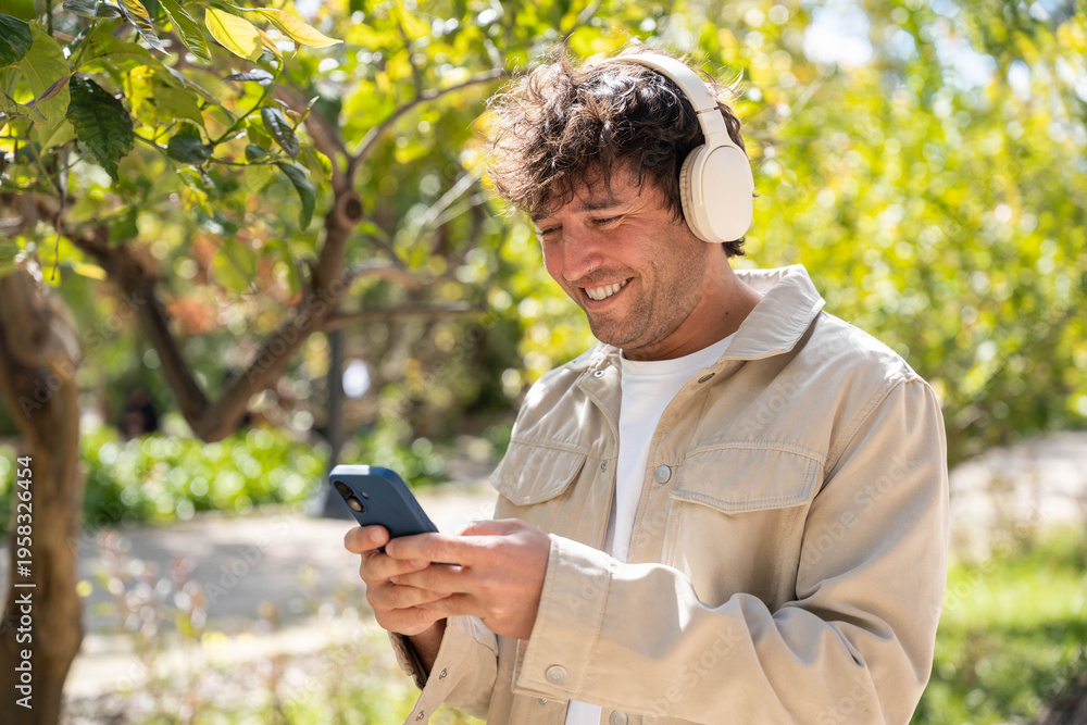 Fototapeta premium A man enjoys listening to music with headphones in a park while using his phone