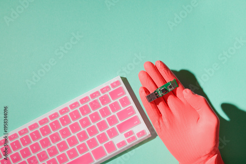 Hand in pink glove holding USB flash drive near pink keyboard, cyber security and data protection concept, mint background, copy space