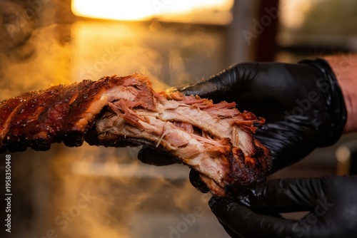 Gloved hands pull apart a rack of smoky barbecue ribs in golden light