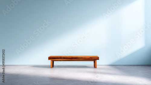 Wooden bench sitting in minimalistic room with light blue wall and concrete floor, casting shadows