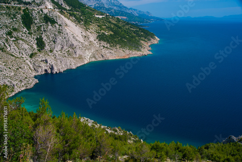 Croatia's picturesque natural landscape. Stunning aerial view of rugged coastline with steep, green-covered mountains descending into deep blue waters, under bright sky.