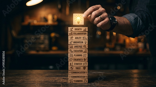 A hand places a glowing lightbulb block on a stack of wooden blocks representing business concepts like growth, innovation, and teamwork, symbolizing new ideas and strategic development.