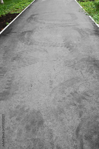 Ahead lies a flat asphalt path bordered by green grass. footprints on the asphalt