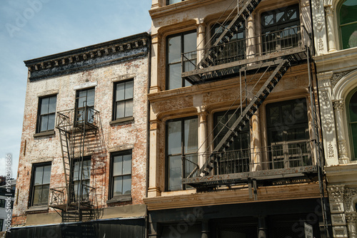 Brick and cast iron buildings with fire escapes line a street in SoHo, New York City. Detailed facades and large windows reflect the historic character of Manhattan architecture.