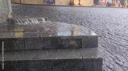 Wet cobblestone street with steps, reflecting light. The scene captures a rainy atmosphere in an urban setting.