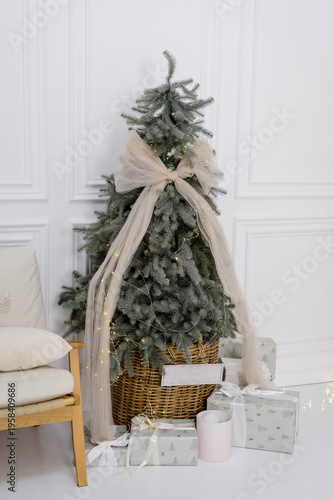 Minimalist Christmas tree in a wicker basket with a large tulle bow, fairy lights, and wrapped gifts in a bright modern interior, ideal for holiday lifestyle and home decor.