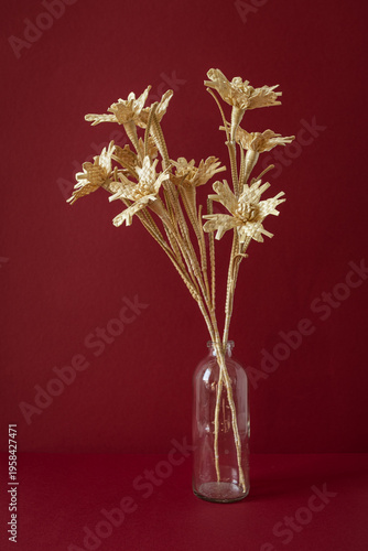 A glass vase with a bouquet of flowers made from straw on the red background. Straw weaving
