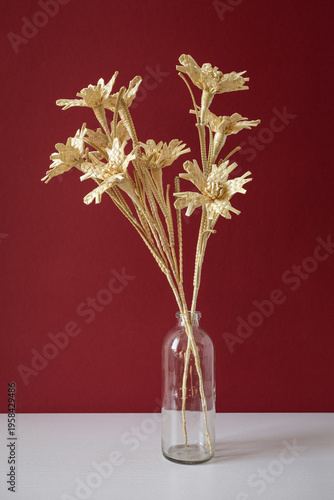 A glass vase with a bouquet of flowers made from straw on the red background. Straw weaving