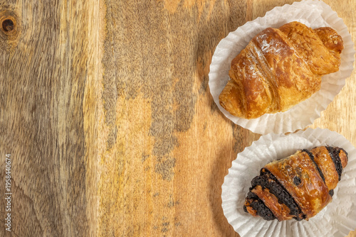Food background with sweet pastry chocolate croissants on paper and wood surface.