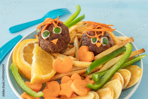 Food ideas for kids. Fresh vegetables, fruits, meat balls in the form of chick, mini pancakes on blue plate.
