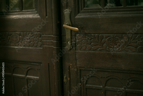 Closeup of carved wooden door handle rich grain and floral carving around brass knob warm brown tones aged patina and panel detail artisan entry