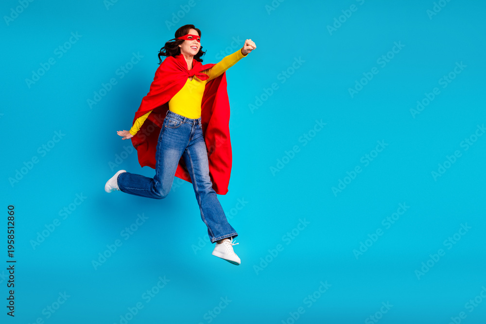 Obraz premium Young woman superhero leaps in bright red cape against blue studio background expressing joy and confidence