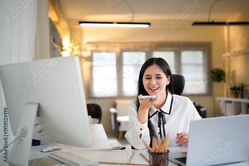 female work by laptop dictate audio message speech on mobile phone voice recording application. Young woman freelance worker talk to client using loudspeaker send voicemail via cell inside office