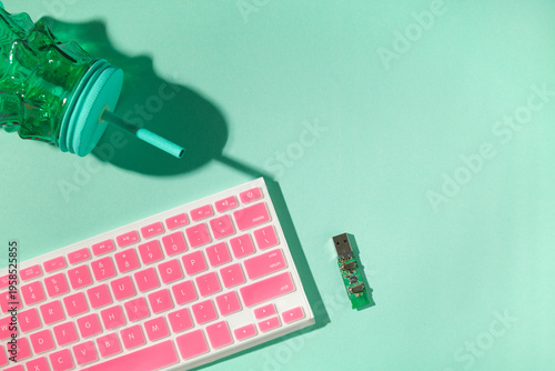 USB board, pink keyboard and green cup with straw on mint background, remote work concept, copy space
