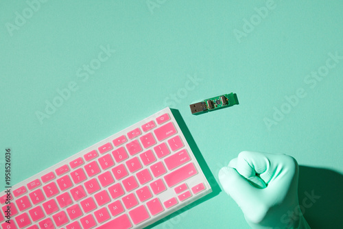Hand in latex glove clenched fist, pink keyboard, USB board, data threat concept, mint turquoise background, overhead view, copy space