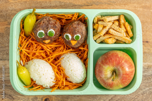 Food background with lunch box of meat balls in the form of chick, rice, carrot salad, fresh apple. Ideas for school lunch box.
