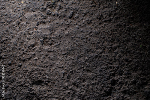 Detailed shot of dark earth ground or asphalt showcasing gritty texture and uneven surface under high contrast side lighting for a dramatic effect.
