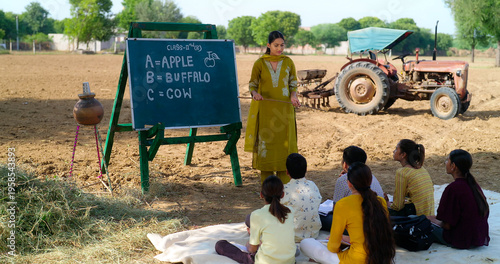 Fotografi Indian young adult gen z female lady talk speak teach to villager child day under tree rural area