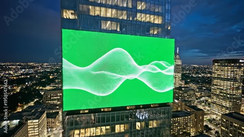 Dynamic green illuminated digital display on a skyscraper at dusk, showcasing fluid wave patterns against a city skyline