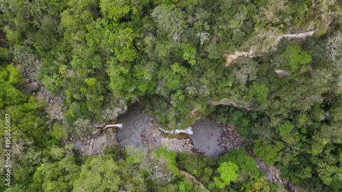 Overhead drone captures two small waterfalls spilling into rock pools beneath a dense green canopy and a winding stream in Villeta, Cundinamarca.