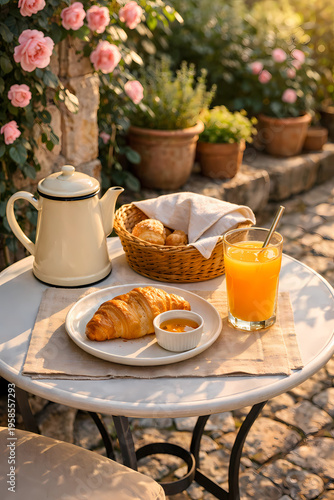 Bistro table on a cobblestone terrace with climbing roses. Croissant with honey, orange juice, enamel coffee pot, and a bread basket. Warm morning light. Terrace dining and summer hosting in an intima