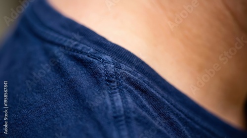 Close up view of a navy blue t shirt's shoulder seam with visible stitching detail against blurred skin