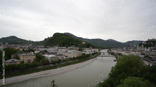 Panoramic View of Salzach River and Kapuzinerberg Hill in Salzburg Austria; Scenic Cityscape with Historic Architecture Bridges and Alpine Landscape under Overcast Sky Establishing Shot