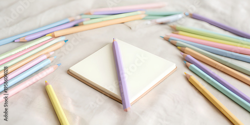 Pastel colored pencils surrounding a blank white notepad