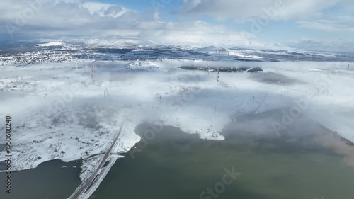 Aerial view of Merom Golan and Bental Reservoir covered in snow with wind turbines rising above the fog, Golan Heights, Israel