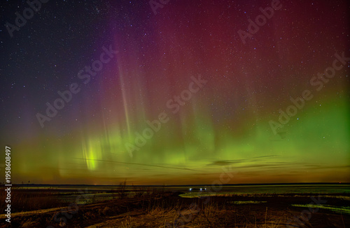 Vivid northern lights dancing over a calm shoreline beneath a star-filled night sky with colorful aurora glow.