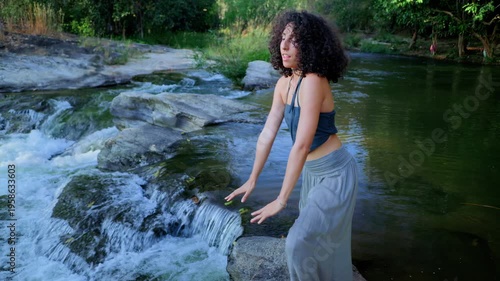 A Serene Moment of Reflection: A Young Woman Engaging in a Meditative Pose by a Tranquil Stream Surrounded by Nature's Beauty and Flowing Water