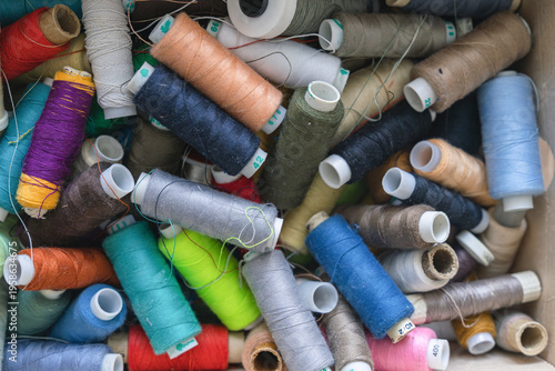 Quadro su tela Various spools of multicolored sewing thread filling a box, creating a textile b