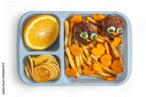 Food ideas for kids. Lunch box with potato chips, heart-shaped carrot, meat balls in the form of chick, fresh orange, cutlery, pancakes on wooden background.
