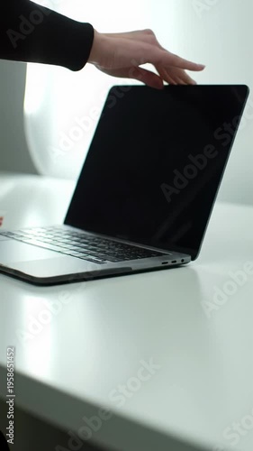 medium video, high-angle view of a well-manicured hand slowly opening a sleek silver laptop with an illuminated screen on a pristine white desk, concept of seamless technology integration