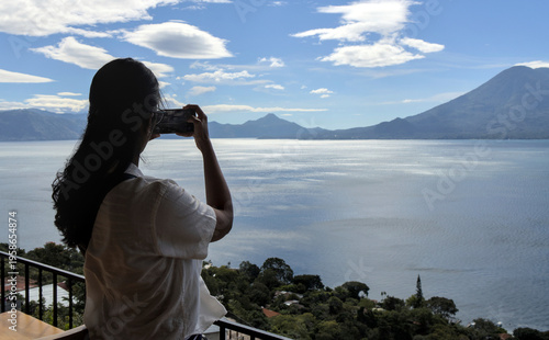 Wallpaper Mural Woman taking a photo of volcanos and mountains at lake atitlan from a restaurant patio. travel, exploration, and nature appreciation Torontodigital.ca