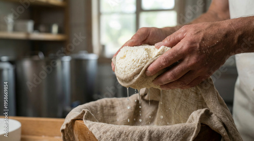 A detailed photo of a pair of hands pressing fresh, crumbly white cheese curds wrapped in a natural linen cheesecloth. Whey drips into a wooden bowl below in a rustic creamery.