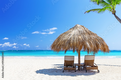 Luxury beach scene with umbrella and lounge chairs on white sand and turquoise ocean in Punta Cana, Dominican Republic.